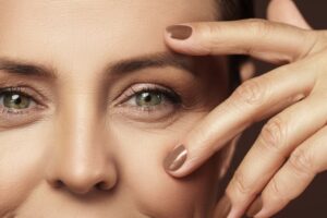 Close-up of a woman's face and left eye. She is holding her hand in front of her cheek and spreading out her fingers to frame her eye.