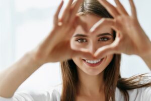 A woman smiling at the camera and making the shape of a heart with her fingers to frame her eyes