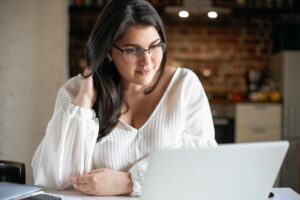 A woman smiling and looking at her laptop, in a cafe setting